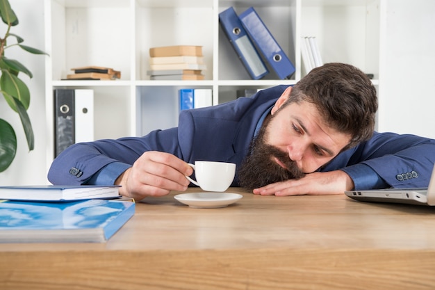 Manhã difícil. Terno formal hippie barbudo relaxante com café. Vida no escritório. Primeiro café. Noite sem dormir. A procrastinação é uma ladra de tempo. Chefe bonito homem dorme no escritório, bebendo café.