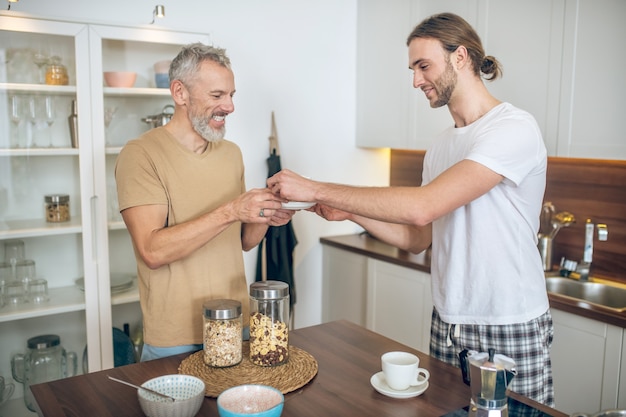 Manhã juntos. Casal sorridente tomando café da manhã juntos em casa e se sentindo bem