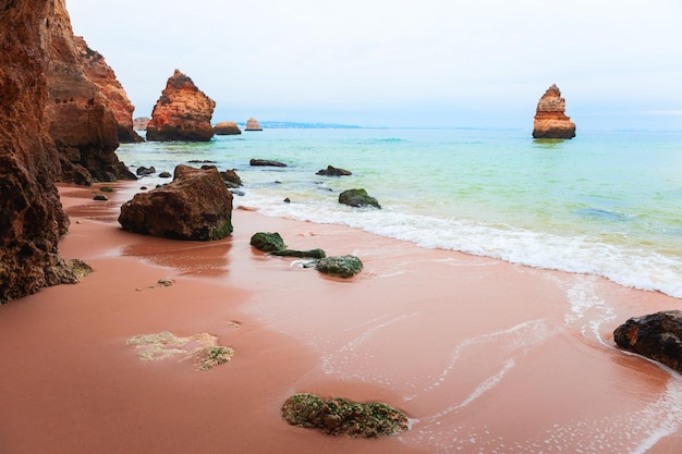 Manhã mística na costa do Oceano Atlântico, no Algarve, Portugal. Areia vermelha com águas turquesas. Destino de viagem famoso