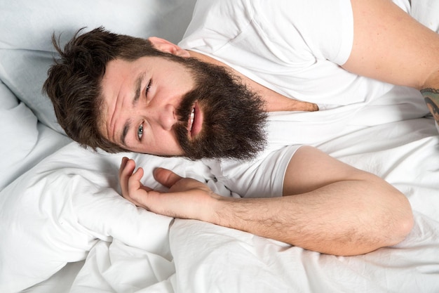 Manhã preguiçosa. Relaxe e durma o conceito. Homem barbudo dorme em lençóis brancos. Sono saudável e bem-estar. Homem barbudo hipster com sono na cama. Primeiras horas da manhã. Insônia e problemas de sono.