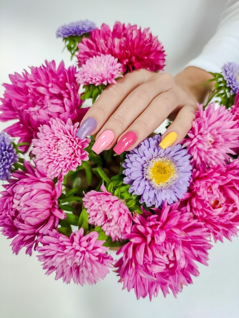 Manicura de colores en uñas largas con un ramo de ásteres.