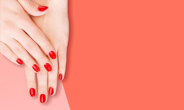 Manicura femenina elegante y de moda. Las manos de una hermosa joven sobre el fondo de Living Coral.