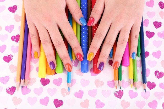 Manicura femenina multicolor con marcadores y lápices sobre fondo brillante