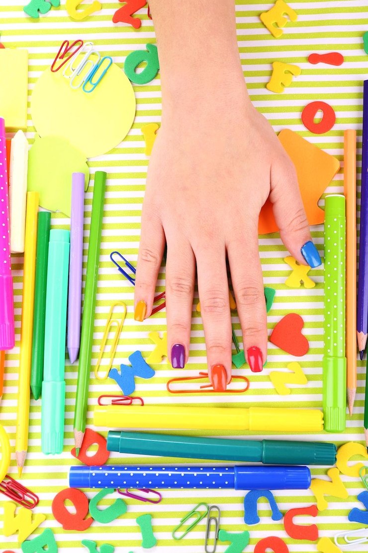 Foto manicura femenina multicolor con papelería sobre fondo brillante.