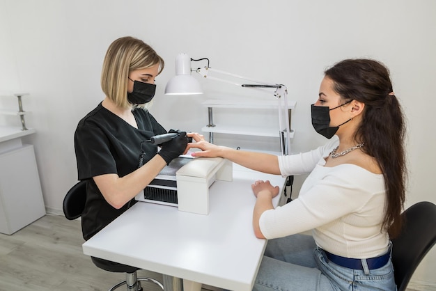 Manicura de hardware en el salón El maestro hace una manicura a una niña en un salón de belleza usando un enrutador El concepto de cuidado profesional de uñas