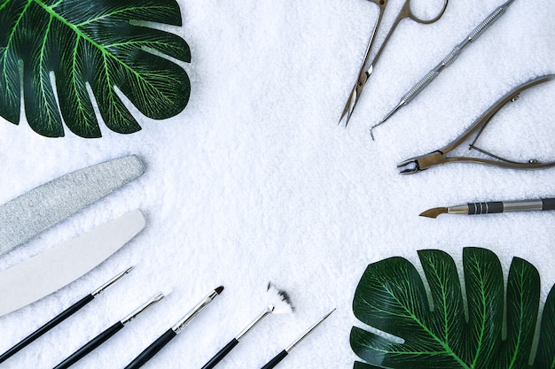 Manicura: herramientas para crear, esmaltes en gel, todo para el tratamiento de las uñas, el concepto de belleza, cuidado con hojas verdes sobre fondo de toalla blanca. Banner para salón de inscripción. Copie el espacio para el texto.