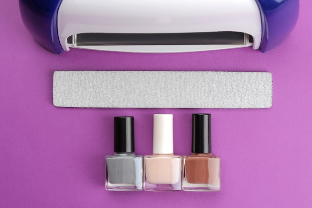 Manicura. Lámpara UV y limas de uñas y esmaltes de uñas sobre un moderno fondo morado. Accesorios y herramientas de manicura para uñas. vista superior