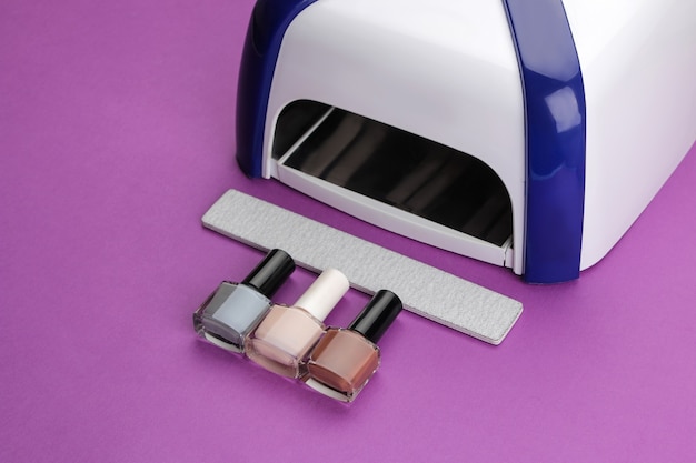 Manicura. Lámpara UV y limas de uñas y esmaltes de uñas sobre un moderno fondo morado. Accesorios y herramientas de manicura para uñas.