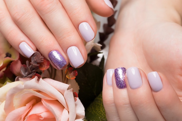 Manicura limpia púrpura en manos femeninas sobre un fondo de flores. Diseño de uñas