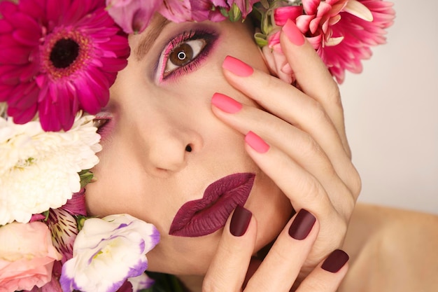 Manicura y maquillaje rosa burdeos en mujer con variedad de flores