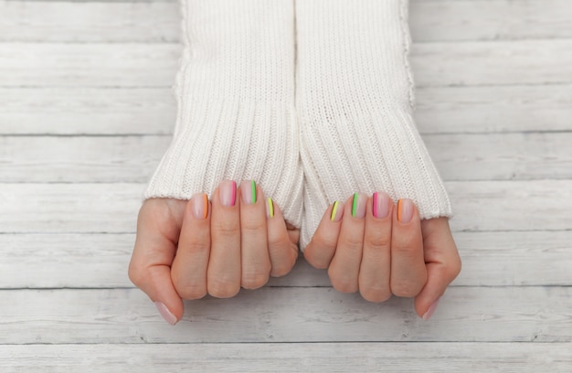 Manicura moderna multicolor, diseño de uñas, estado de ánimo de verano, manos en una vista superior de suéter blanco