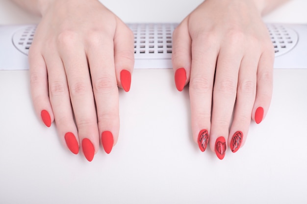 Manicura roja con un patrón. Manos femeninas en salón de manicura