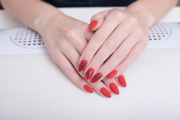 Manicura roja con un patrón. Manos femeninas en salón de manicura