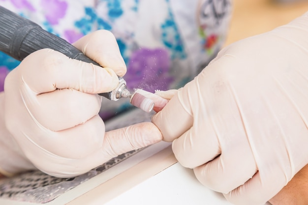 La manicura utiliza una máquina de uñas eléctrica para quitar las manos del esmalte de uñas en el salón de uñas. Concepto de salud y belleza.