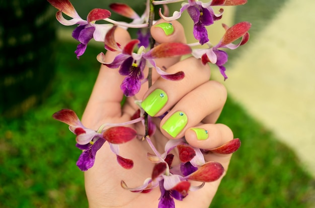 Manicura verde con hermosas flores de orquídeas