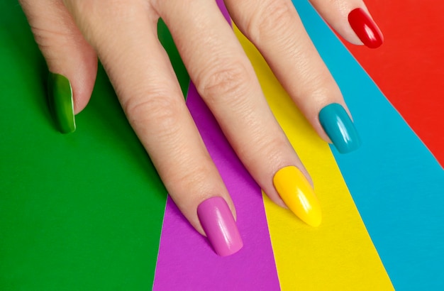 Foto manicure brilhante multicolorida com diferentes formas de unhas quadradas, ovais e afiadas em um fundo colorido.