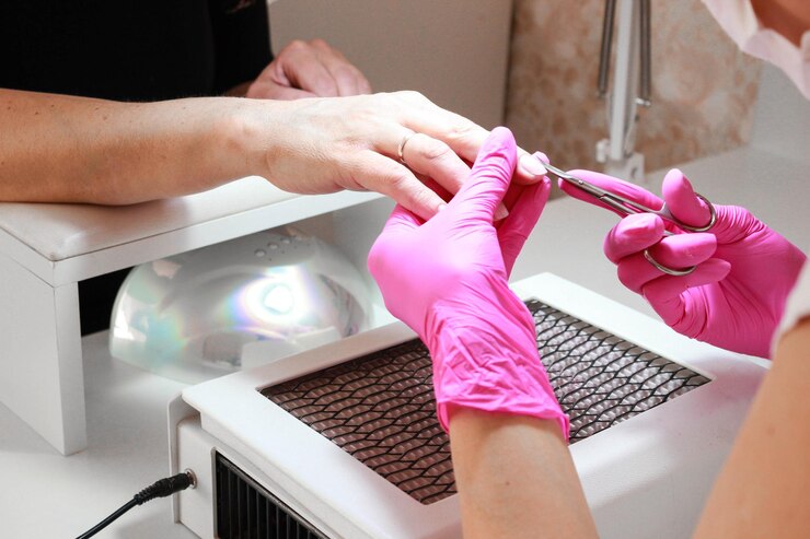 Foto manicure com luvas rosa faz uma manicure aparada com uma tesoura corta a cutícula.
