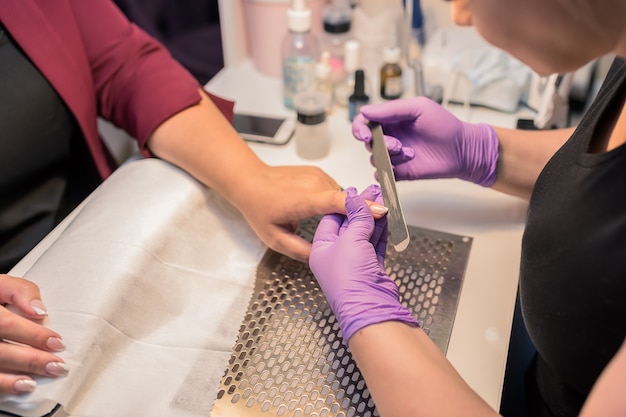 Manicure de hardware em um moderno salão de beleza. O cosmetologista com uma máscara facial rosa faz o procedimento cosmético para a cliente loira, o local de trabalho profissional em segundo plano