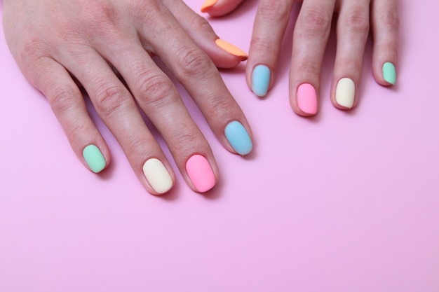 Manicure fosca colorida nas mãos femininas em um fundo rosa com espaço de cópia