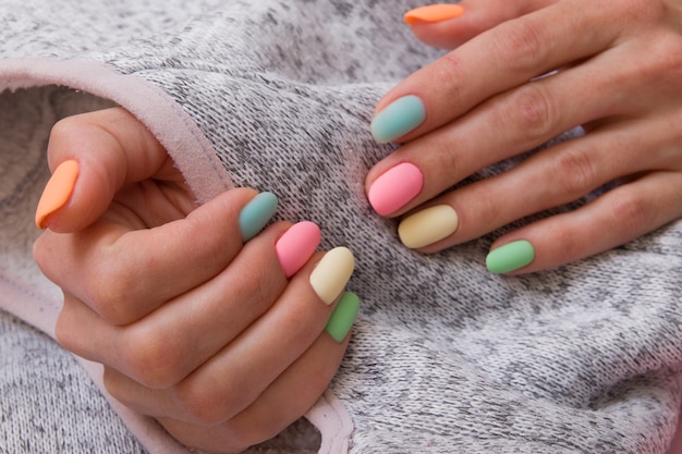 Manicure fosca colorida nas mãos femininas em uma superfície cinza