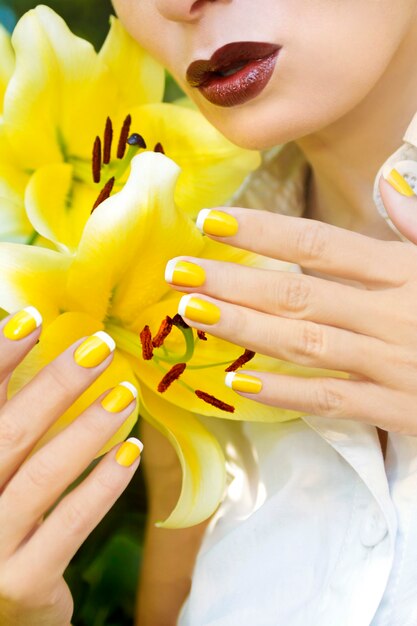 Manicure francesa amarela para a menina com os lírios amarelos no close up do verão.