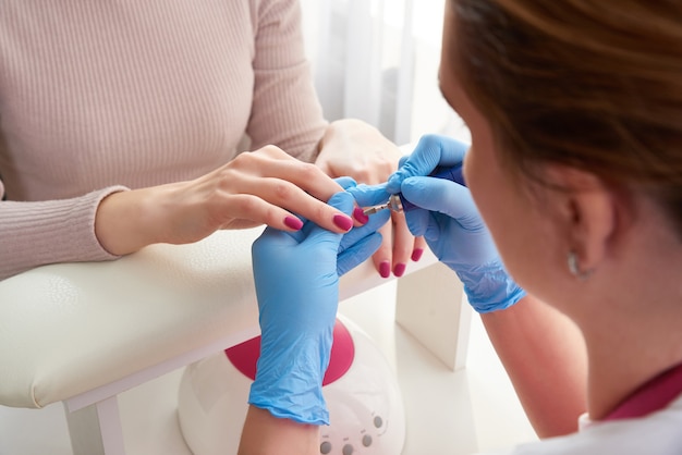 Foto manicure master utiliza una máquina de uñas eléctrica para quitar las manos de esmalte de uñas en el salón de uñas