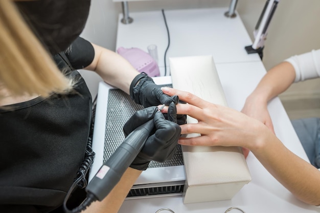 Manicure mulher remove gel de goma-laca das unhas do cliente usando máquina de manicure Manicure trabalha com uma furadeira elétrica em um salão de beleza O processo de manicure de hardware