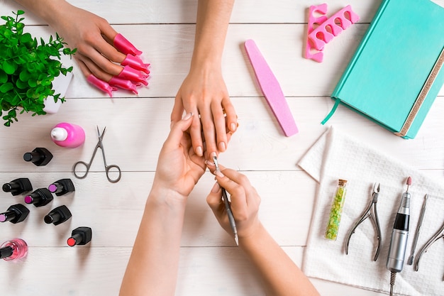 Manicure para o cliente, close up das mãos de uma manicure e cliente em um fundo de madeira