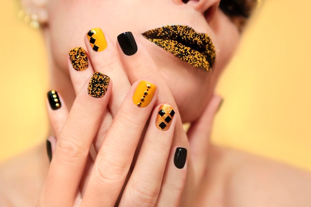 Manicure preto e amarelo com strass e maquiagem