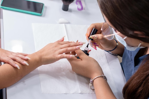 Manicure profissional aplicando uma camada de base transparente nas unhas de uma mulher