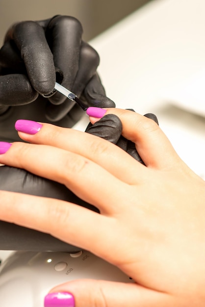 Foto manicure profissional uma manicure está pintando as unhas femininas de um cliente com esmalte roxo em um salão de beleza close-up conceito da indústria de beleza