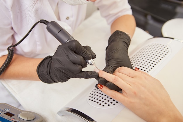 Manicure removendo cutícula na mão de uma mulher com uma broca de unha elétrica