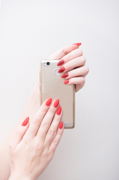 Manicure vermelha com um padrão. Telefone inteligente na mão feminina. fundo branco