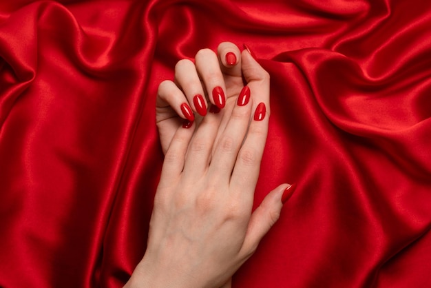 Manicure vermelha nas mãos da mulher em um fundo de seda vermelho de luxo