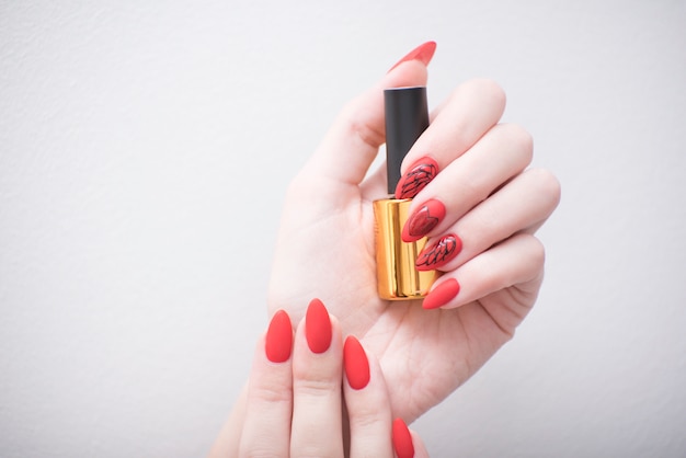 Manicure vermelho com um padrão. Frasco com esmalte