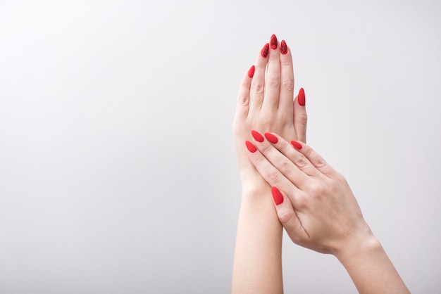Manicure vermelho com um padrão. Mãos femininas em um branco