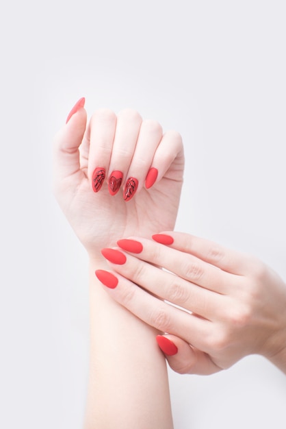 Manicure vermelho com um padrão. Mãos femininas em um fundo branco