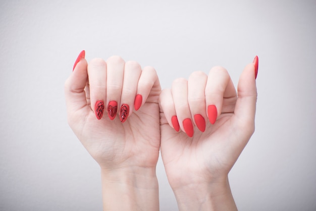 Manicure vermelho com um padrão. Mãos femininas em uma parede branca