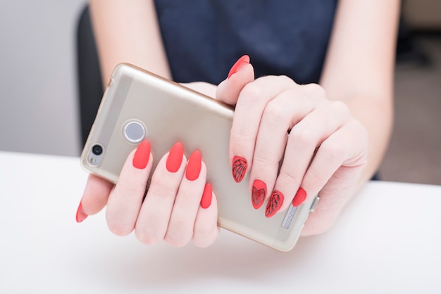 Manicure vermelho com um padrão. Telefone inteligente na mão feminina.