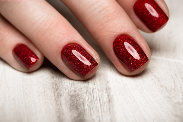 Manicure vermelho festivo brilhante nas mãos femininas. Desenho de unhas.