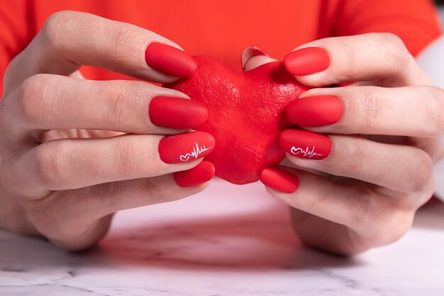 Manicure vermelho fosco nas mãos femininas para o dia dos namorados