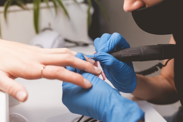 Manicurist limpia las uñas con un taladro de lima de uñas antes de aplicar el barniz