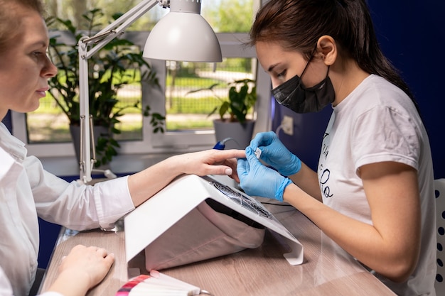 La manicurista afila las uñas de la clienta con una lima especial sobre la aspiradora que está en la mesa de manicura