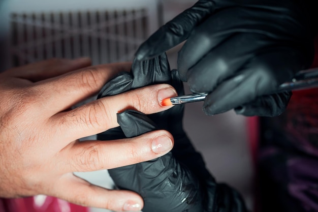 Manicurista aplica esmalte de uñas en las uñas de los hombres en un spa vista de cerca desde arriba