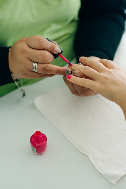 Manicurista aplicando esmalte de uñas rosa a las uñas de una clienta en un spa o salón de belleza