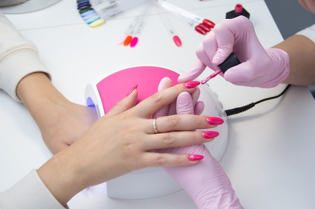 Manicurista aplicar esmalte de uñas. Primer plano de una mujer aplicando esmalte de uñas en las uñas. Uñas rosas.