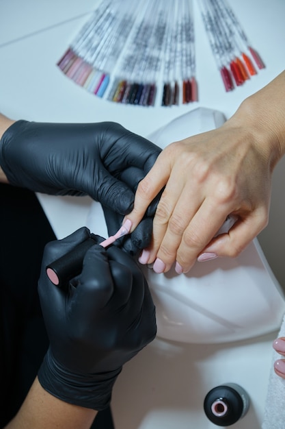 Foto manicurista barniza las uñas de gel. cuidado profesional de manos y uñas en salón de belleza