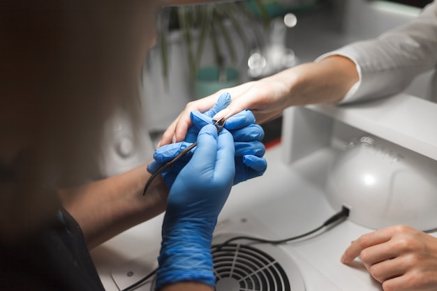 Manicurista corta la cutícula en las uñas del cliente con una pinza