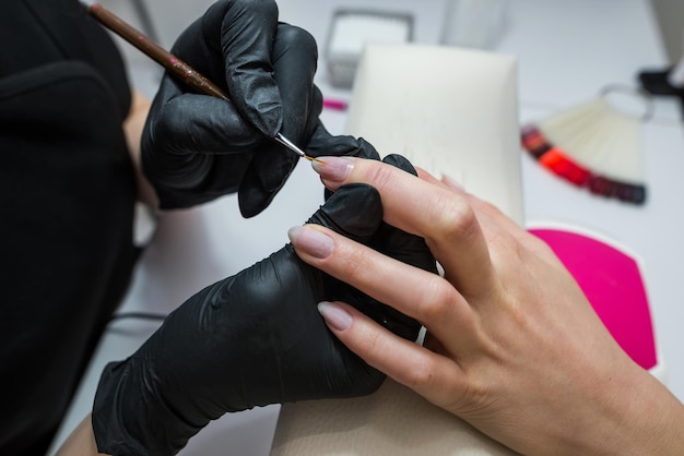 La manicurista cubre las uñas del cliente con barniz rojo Manicura en un salón de belleza Concepto de cuidado de uñas