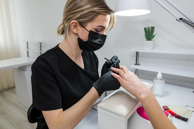 La manicurista cubre las uñas del cliente con barniz rojo Manicura en un salón de belleza Concepto de cuidado de uñas